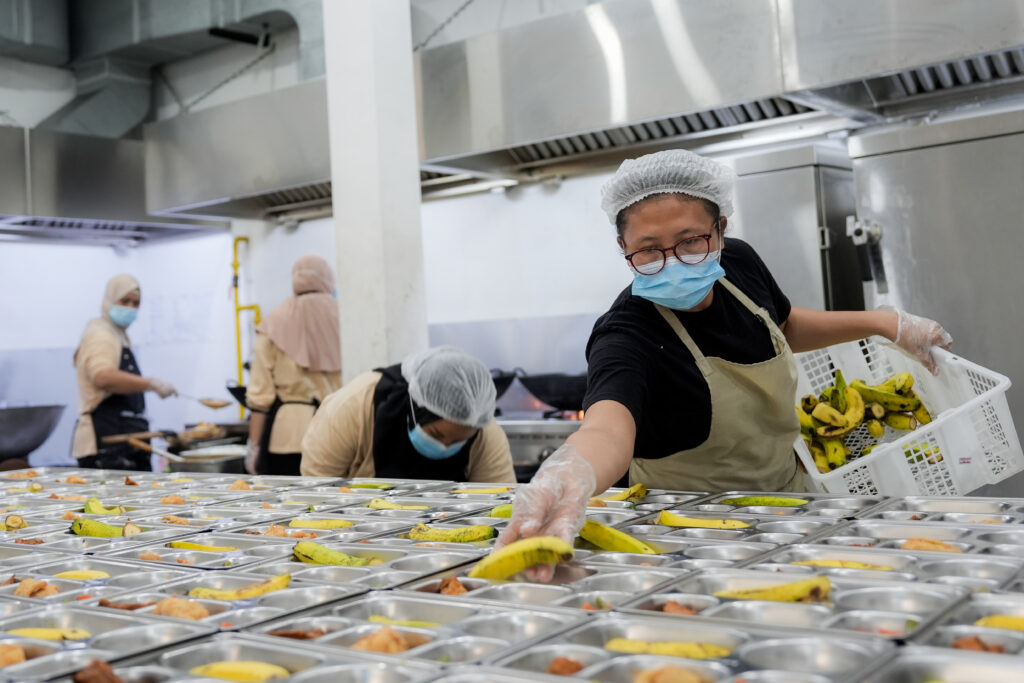 Ilustrasi kegiatan pengemasan makanan di dapur Makan Bergizi Gratis (MBG) pada sebuah Satuan Pelayanan Pemenuhan Gizi (SPPG). Foto: Ist.